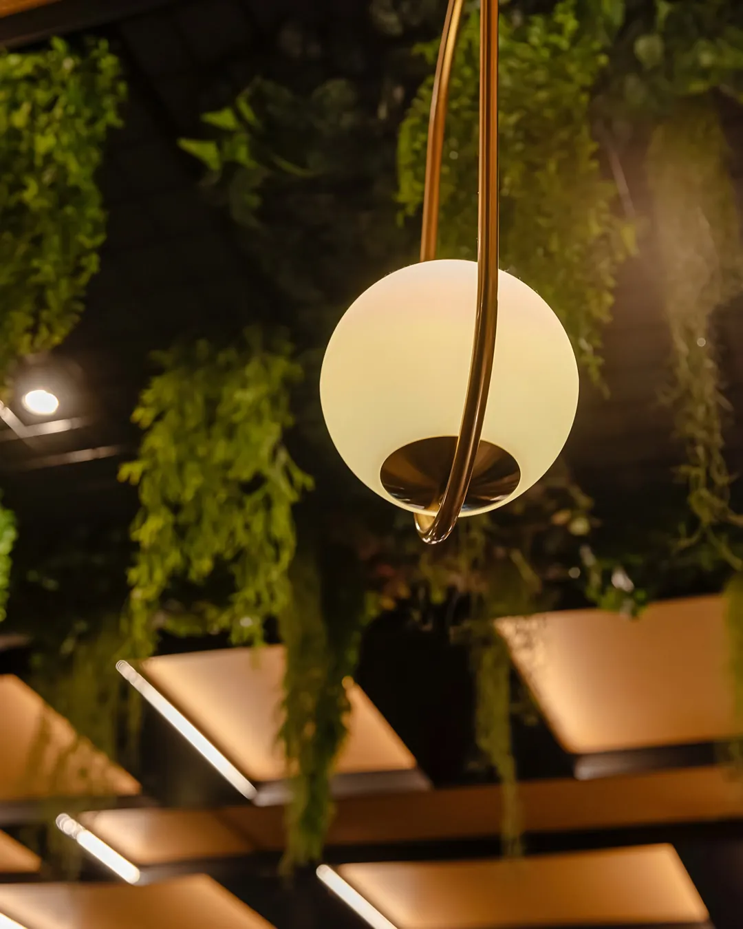 Una lampada dorata sospesa tra le piante della sala